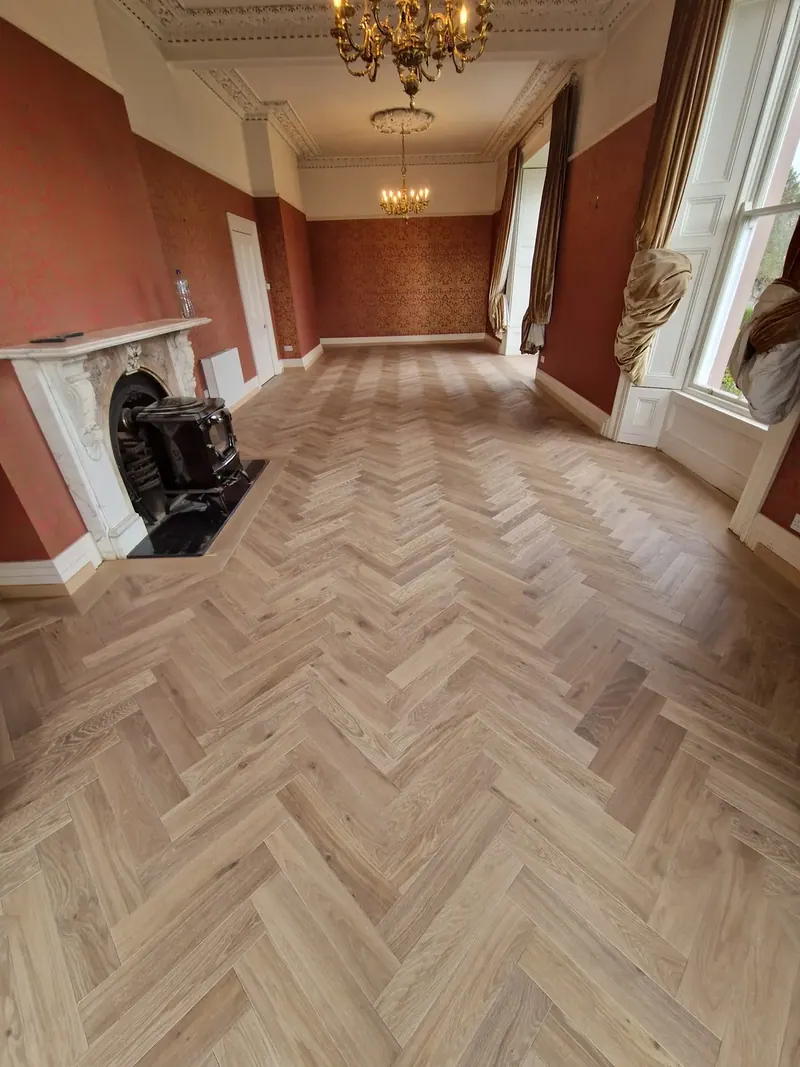 Herringbone floor in a period room with a marble fireplace and chandelier
